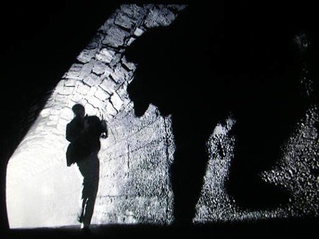 Black & white image of a man running through an illuminated tunnel.